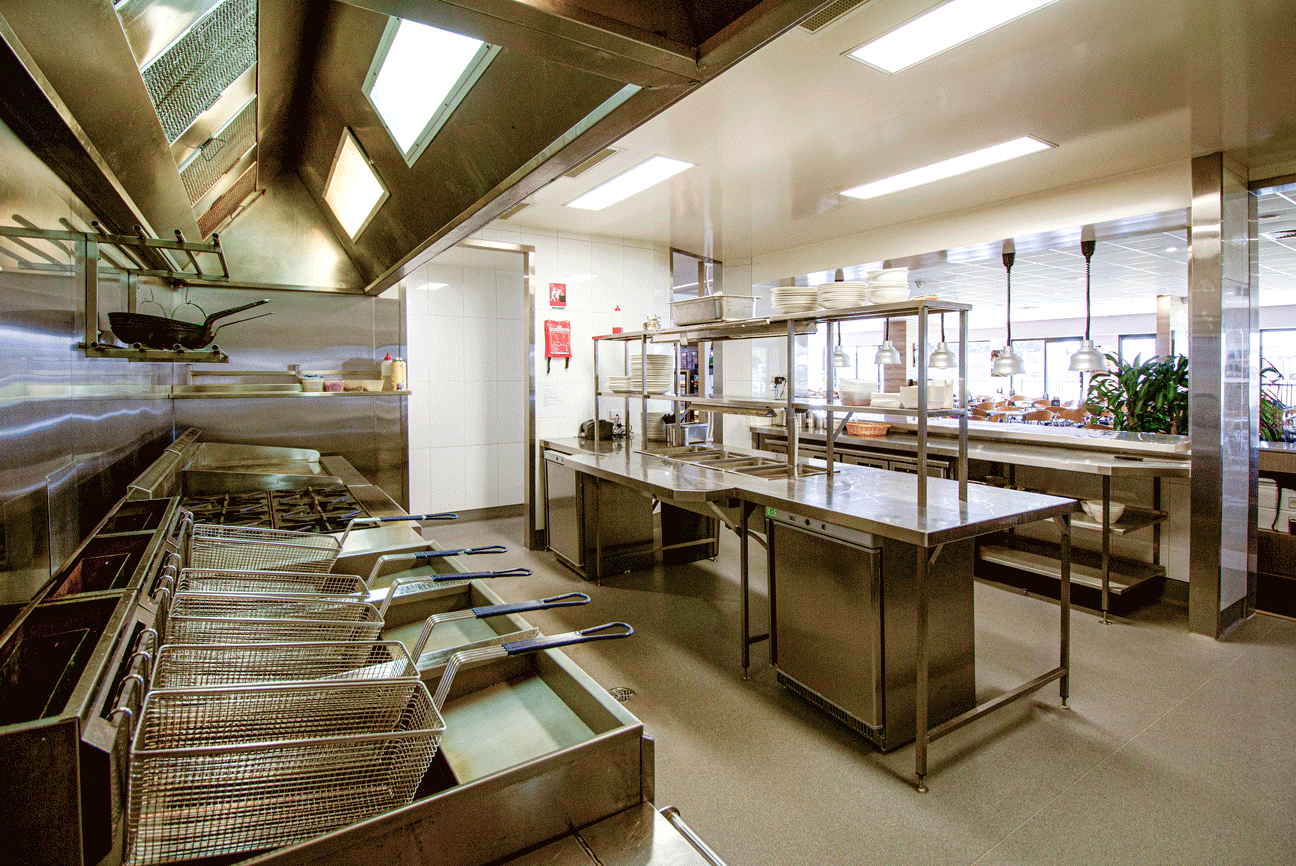 A well-equipped commercial kitchen featuring stainless steel surfaces, overhead range, and gas fryers, designed in light brown and maroon hues, portraying cleanliness and efficiency.